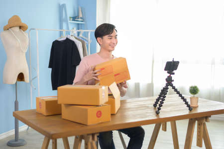 An Asian man is showing clothes in front of smartphone  live streaming at his shop. Technology...