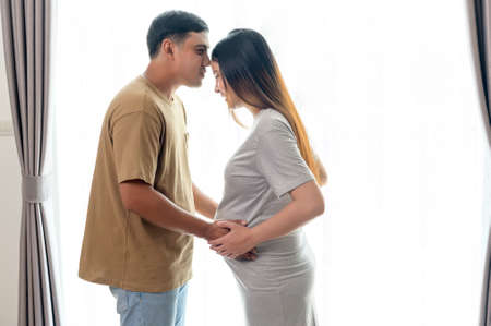 Young pregnant woman with husband embracing and expecting a baby at homeの写真素材