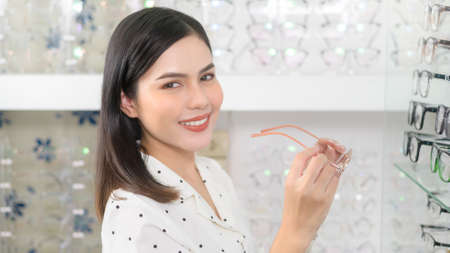 A young female customer choosing glasses in optical center, Eyecare concept.