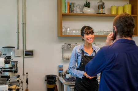 Young service minded barista woman with customer in coffee shop
