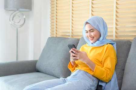 A Young happy muslim woman relaxing and using smartphone in living room.
