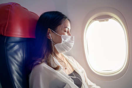 A Young woman wearing face mask is using smartphone onboard, New normal travel after covid-19 pandemic conceptの写真素材
