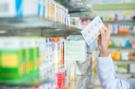 A Female pharmacist wearing lab coat in a modern pharmacy drugstore., selecting a medicine for customer.の写真素材