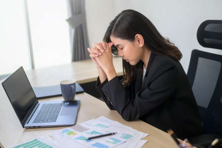 A Stressed young business woman working on laptop with documents in modern office, workload conceptの写真素材