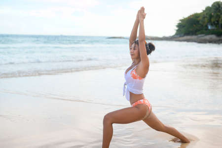 A Young asian woman in bikini doing yoga on the beach, health and meditation conceptの写真素材