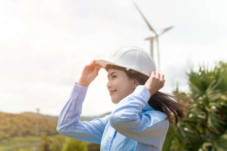 Female engineer working on the seaside wearing a protective helmet over electrical turbines background.の写真素材