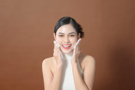 A young woman with beautiful face smiling, washing her face over brown background , beauty skin care conceptの写真素材