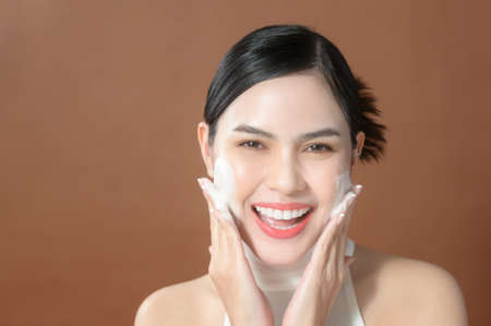 A young woman with beautiful face smiling, washing her face over brown background , beauty skin care conceptの写真素材