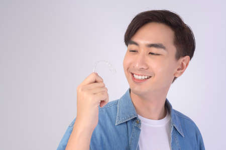 A Young smiling man holding invisalign braces over white background studio, dental healthcare and...