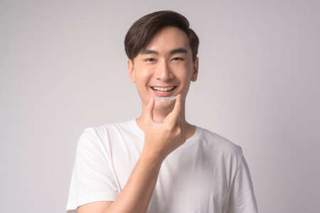 A Young smiling man holding invisalign braces over white background studio, dental healthcare and Orthodontic concept.の写真素材