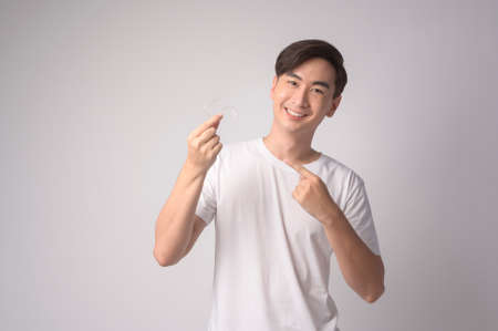 A Young smiling man holding invisalign braces over white background studio, dental healthcare and...