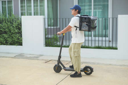 A Smiling delivery man with thermal backpack riding on an electric scooter, deliver online conceptの写真素材