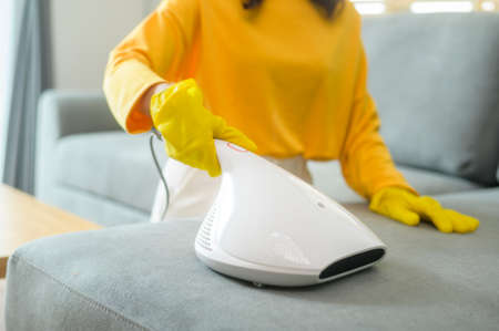 Young happy woman wearing yellow gloves  and vacuum Cleaning a sofa in living room.の写真素材