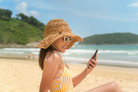A Young Beautiful woman in Bikini listening to music and using smartphone on the beach,  Summer,...