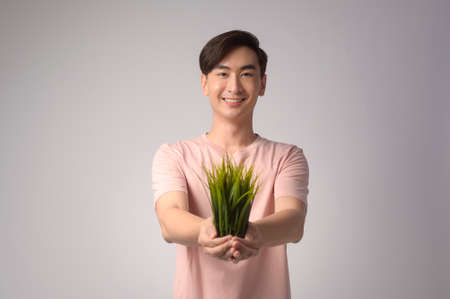 A Young smiling man holding tree over white background studio, save earth conceptの写真素材