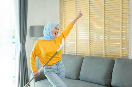 A Young happy muslim woman mopping and vacuum the floor in living room.