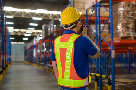 A Young asian male worker wearing helmet using talki walki in modern warehouse.の写真素材