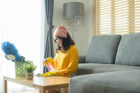 A Young happy woman wearing yellow gloves  and dusting the table in living room.の写真素材