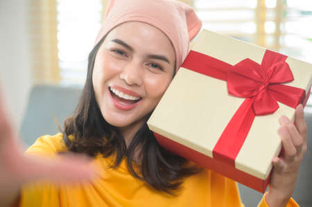 A Young surprised woman opening a gift box in living room.の写真素材