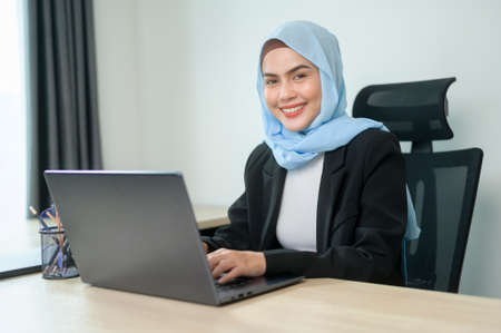 A Young muslim business woman working on laptop with documents in modern office