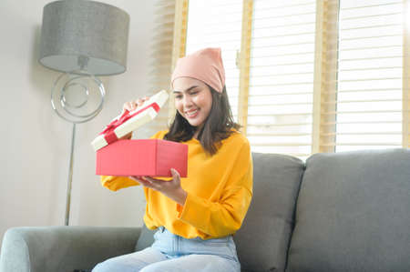 A Young surprised woman opening a gift box in living room.の写真素材