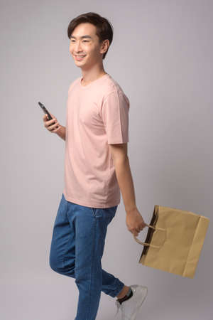 A Young asian man holding smartphone and shopping bag over white background studio, shopping and finance concept.の写真素材