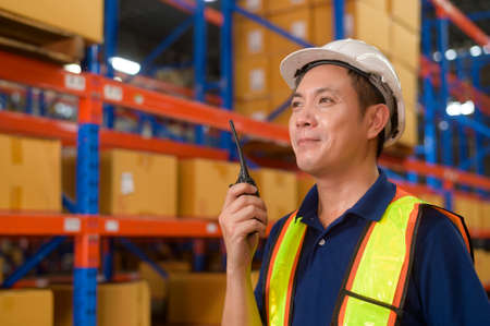 A Young asian male worker wearing helmet using talki walki in modern warehouse.の写真素材