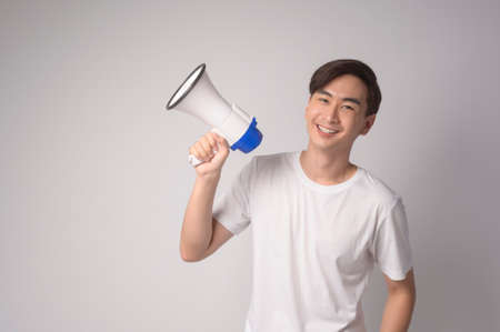 A young smiling man holding megaphone over white background studio.の写真素材
