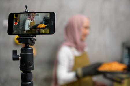 A Beautiful muslim woman is making bakery while live streaming or recording video on social media in...