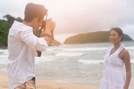 A Happy young couple wearing white dress enjoy taking photo on the beach on holidays, travel,...