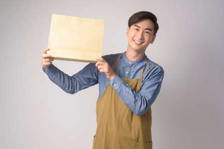 A Portrait of young asian man wearing apron holding paper bag over white background studio, Save earth concept.の写真素材