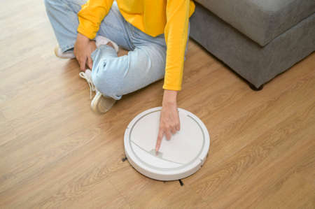 A Young happy woman using Robotic vacuum cleaner in living room