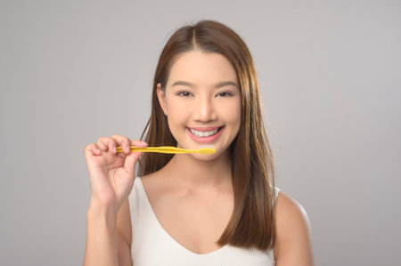 A Young smiling woman holding toothbrush over white background studio, dental healthcare and...