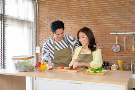 A Young smiling asian couple wearing an apron in the kitchen room, cooking conceptの写真素材