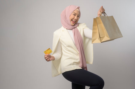 A Beautiful muslim woman with hijab holding credit card over white background studio, shopping and...