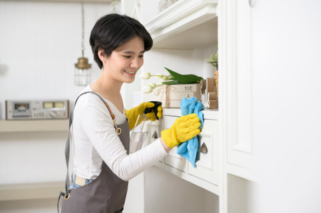 An Asian woman with cleaning gloves using alcohol spray sanitiser to cleaning house, healthy...