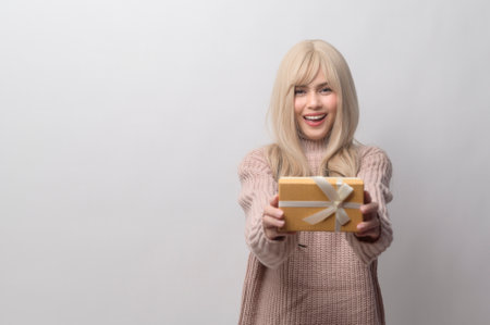 Portrait of Caucasian young woman wearing sweater holding gifts box  over white backgroundの写真素材