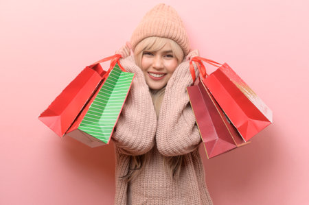 Portrait of Caucasian young woman wearing sweater holding  shopping bag over pink backgroundの写真素材
