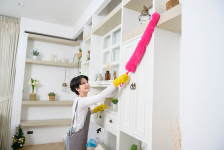Happy Asian young woman sweeping sofa and furniture to cleaning house, healthy lifestyle conceptの写真素材