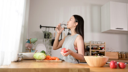 An Asian young woman drinking fresh water in kitchen at home , healthy lifestyle concept
