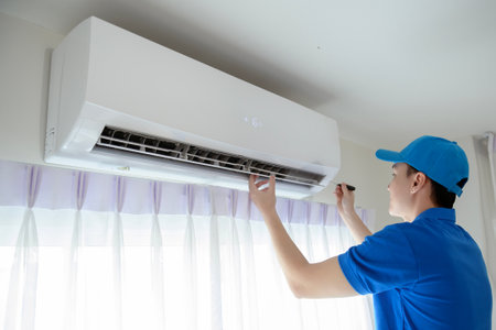 An Asian young Technician service man wearing blue uniform checking ,  cleaning air conditioner in homeの写真素材