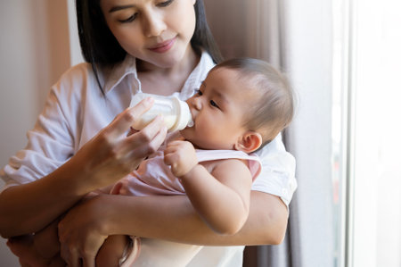 A baby girl is drinking milk bottle in mother arms, family, child, childhood and parenthood conceptの写真素材