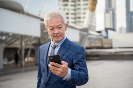 Asian senior mature middle aged businessman using smartphone in modern cityの写真素材