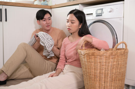 Asian young couple doing laundry together feeling tried , bored , arguing about the relationship problem .の写真素材