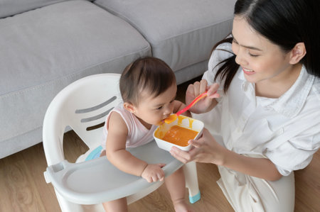 A Young mother helping baby eating blend food on baby chair