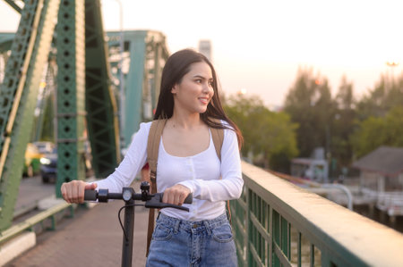 Portrait of young beautiful woman with an electric scooter  over bridge in modern city  backgroundの写真素材