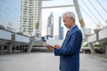 Asian senior mature middle aged businessman using tablet in modern cityの写真素材