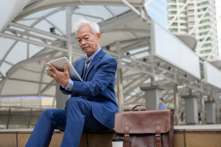 Asian senior mature middle aged businessman using tablet in modern cityの写真素材
