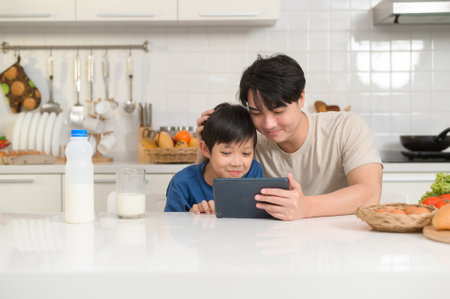 Young Asian father and his son using digital tablet enjoying together in kitchen at homeの写真素材