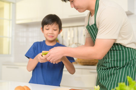 Happy Young Asian father making breakfast to his son in kitchen at homeの写真素材